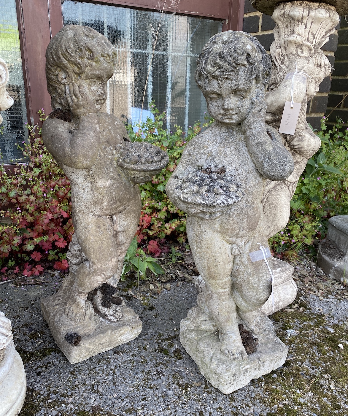 A pair of reconstituted stone garden ornaments, cherubs with fruit baskets, height 72cm